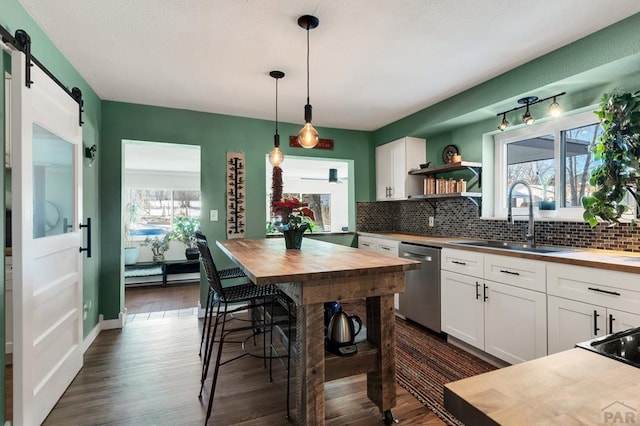 kitchen with a barn door, white cabinets, stainless steel dishwasher, open shelves, and a sink