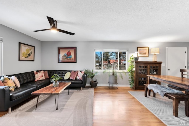 living area featuring a ceiling fan, baseboards, light wood-style flooring, and a textured ceiling