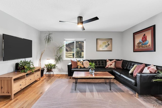 living area with ceiling fan, a textured ceiling, baseboards, and wood finished floors