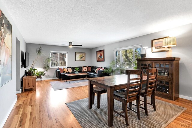 dining space featuring light wood-style floors, ceiling fan, a textured ceiling, and baseboards