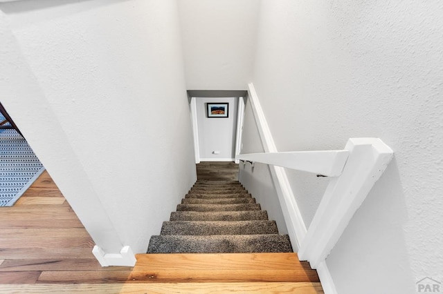 stairs featuring wood finished floors and a textured wall