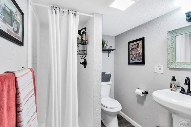 bathroom featuring a textured wall, toilet, wood finished floors, curtained shower, and a sink