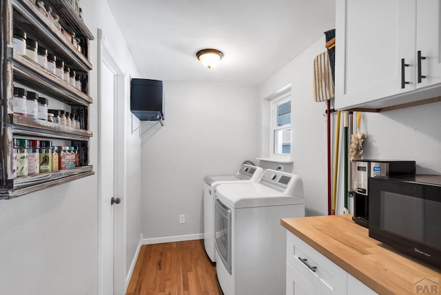 laundry room featuring cabinet space, washing machine and dryer, light wood-style flooring, and baseboards