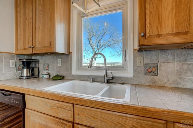 kitchen with black dishwasher, tile countertops, backsplash, and a sink