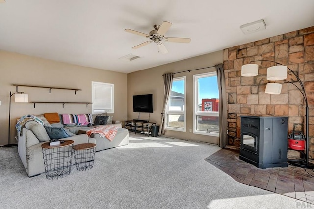 living room featuring a wood stove, ceiling fan, visible vents, and carpet floors