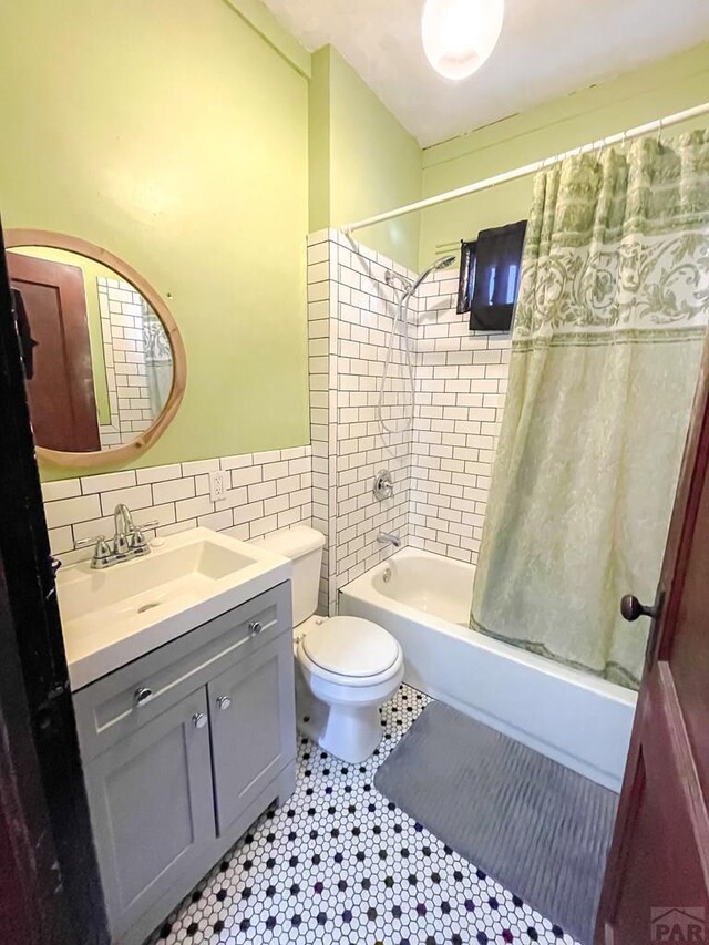 full bath with toilet, vanity, tile walls, tile patterned floors, and shower / bath combination with curtain