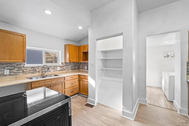 kitchen with stove, a sink, washer and dryer, light countertops, and backsplash