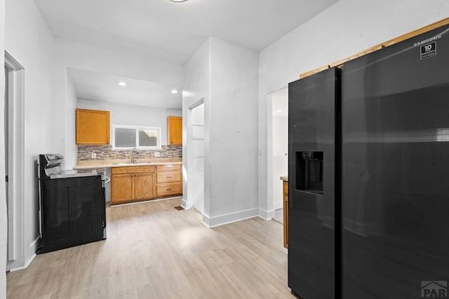 kitchen featuring light countertops, electric range oven, a sink, light wood-type flooring, and black fridge