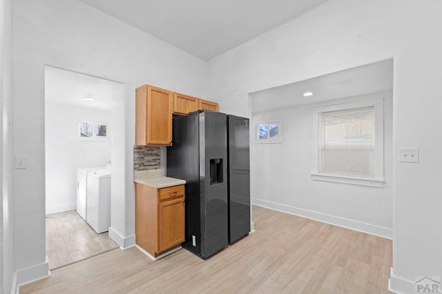 kitchen with light countertops, black refrigerator with ice dispenser, light wood-style flooring, and washer and dryer