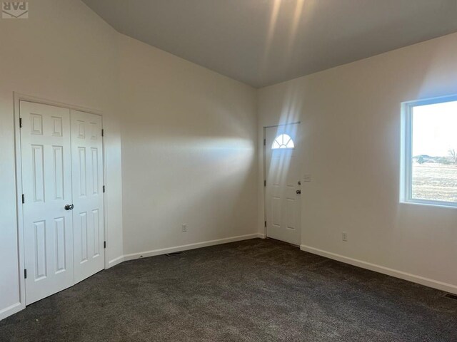 unfurnished room featuring dark colored carpet and baseboards