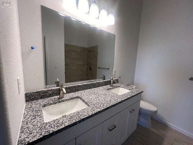 full bath with tiled shower, a sink, toilet, and double vanity