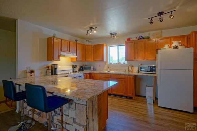 4131 County Rd 510, Walsenburg, CO 81055 - kitchen with a sink, wood finished floors, a peninsula, under cabinet range hood, and white appliances