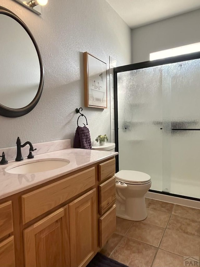 bathroom with a textured wall, tile patterned flooring, a shower stall, and toilet