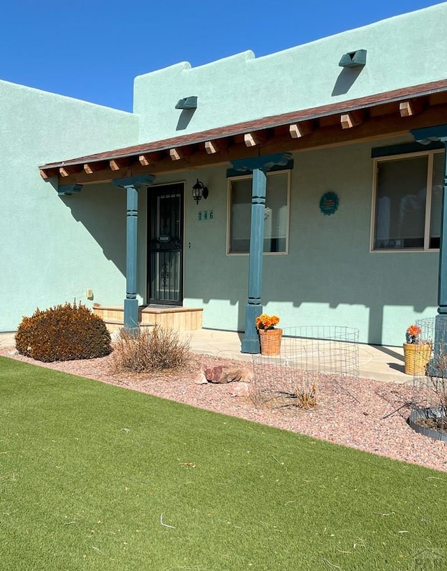 property entrance featuring a porch, a lawn, and stucco siding