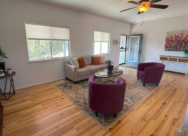 living room with baseboards, visible vents, a ceiling fan, and light wood-style floors