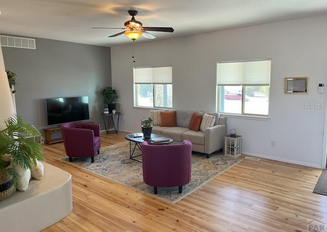 living area featuring baseboards, wood finished floors, visible vents, and a ceiling fan