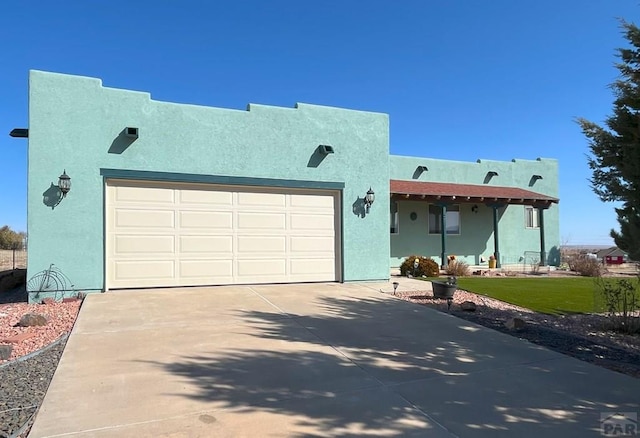 pueblo-style home with a garage, a front yard, concrete driveway, and stucco siding