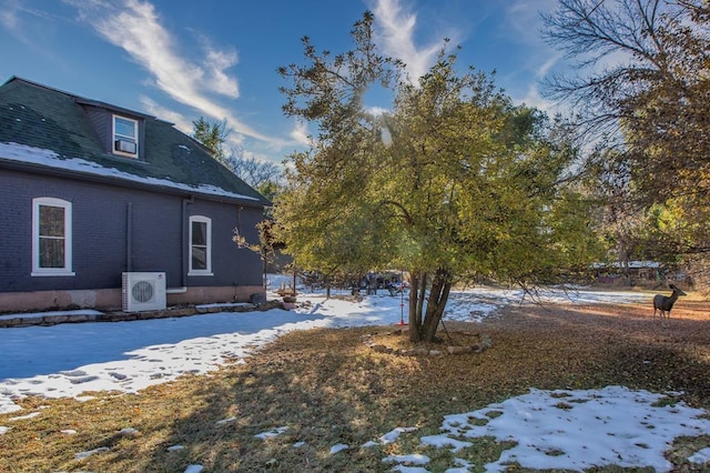 snow covered property with ac unit and brick siding