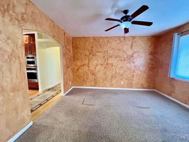 spare room with baseboards, carpet, arched walkways, and a ceiling fan