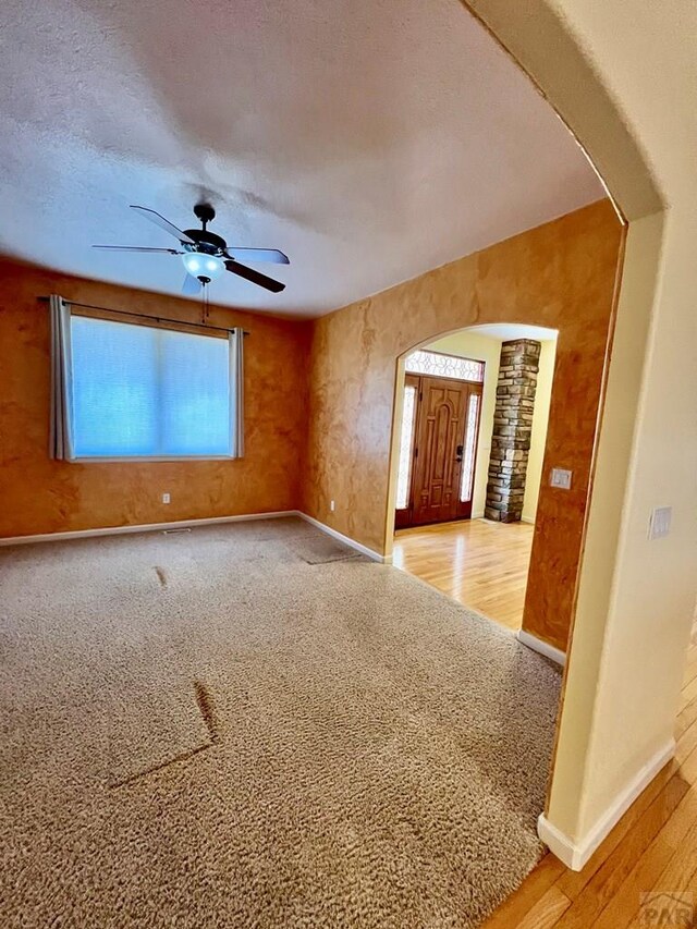 empty room featuring arched walkways, ceiling fan, a textured ceiling, and baseboards