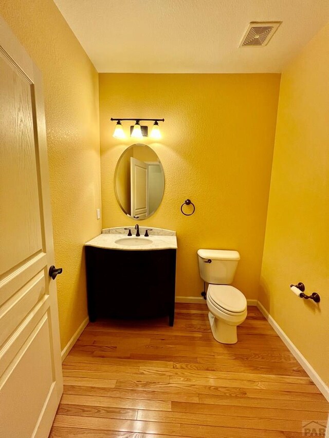 half bathroom featuring visible vents, toilet, vanity, wood finished floors, and baseboards