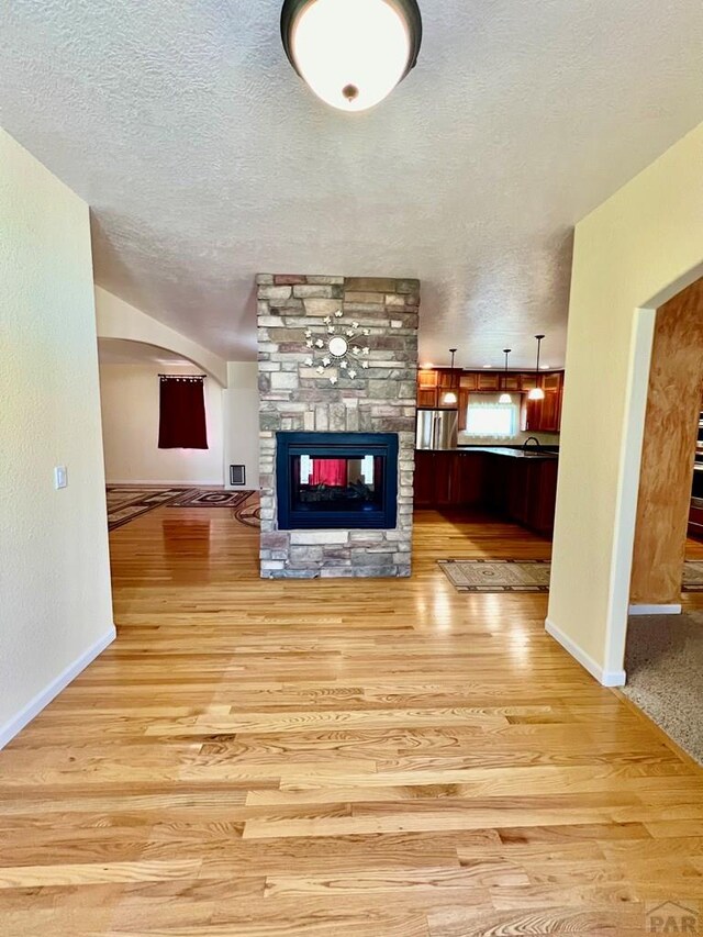 living room featuring light wood-style floors, arched walkways, a stone fireplace, and a textured ceiling