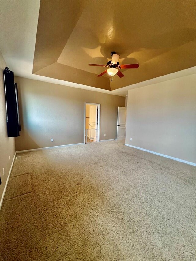 unfurnished room featuring a tray ceiling, carpet, and baseboards