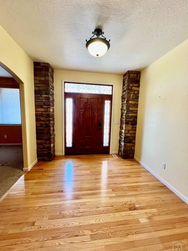 entryway with arched walkways, baseboards, a textured ceiling, and light wood finished floors