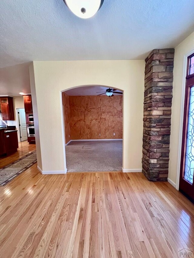 interior space featuring light wood-style floors, baseboards, arched walkways, and a textured ceiling