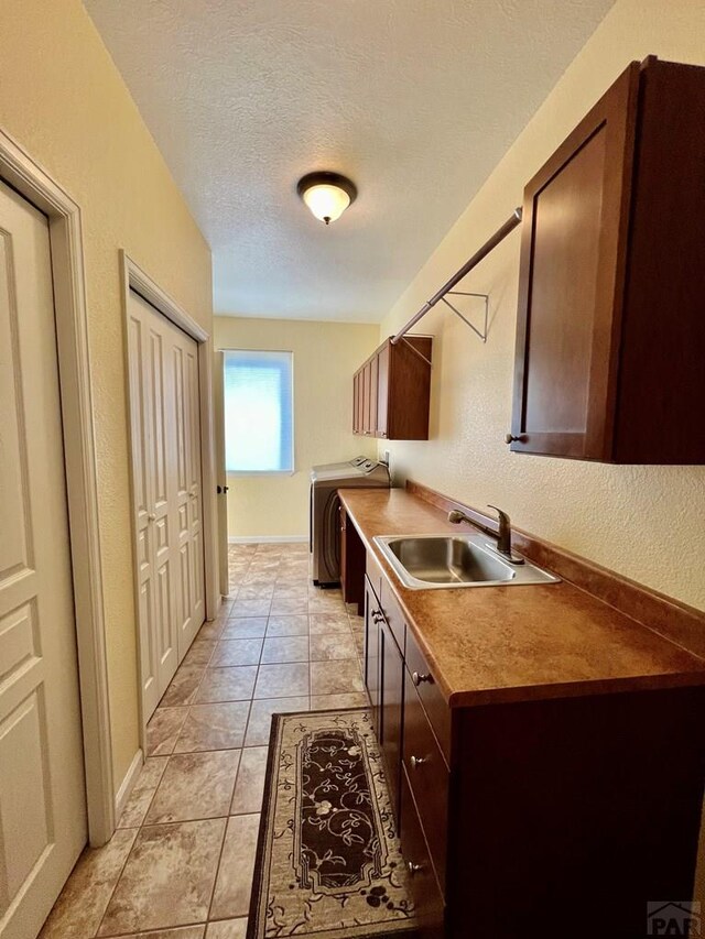 kitchen featuring a textured ceiling, light tile patterned floors, a sink, dark brown cabinets, and washer / clothes dryer