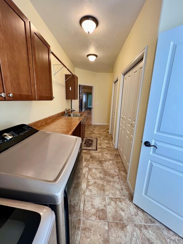 washroom with a textured ceiling, a sink, baseboards, cabinet space, and washing machine and clothes dryer