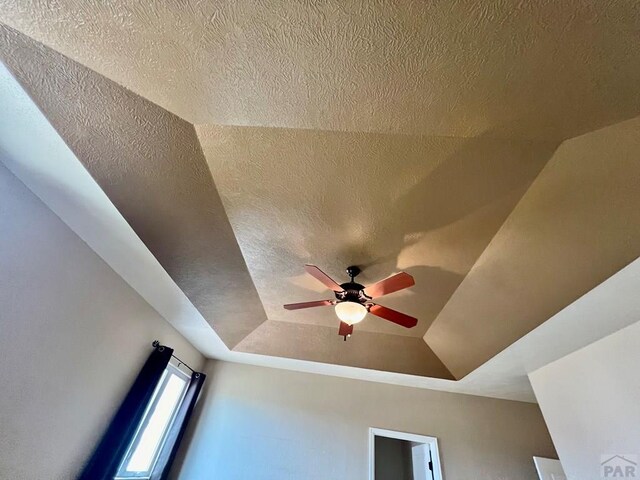 interior details featuring ceiling fan, a textured ceiling, and a raised ceiling