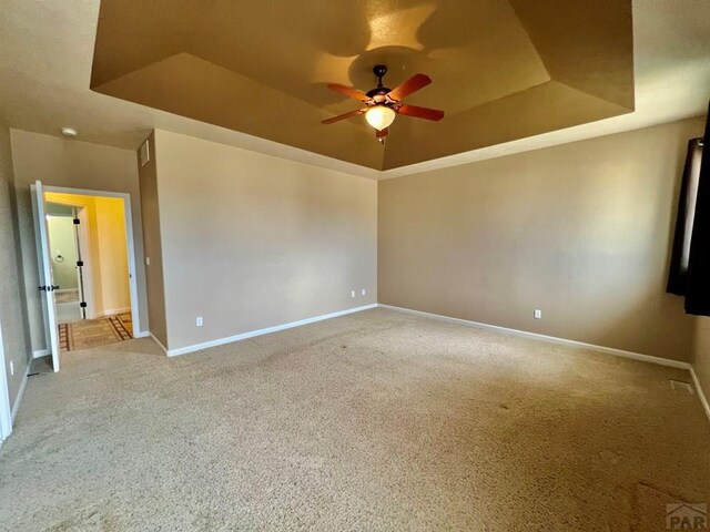 spare room with light carpet, ceiling fan, a tray ceiling, and baseboards