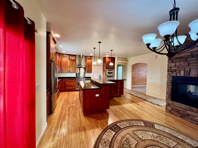 kitchen featuring dark countertops, high quality appliances, open floor plan, hanging light fixtures, and wall chimney range hood