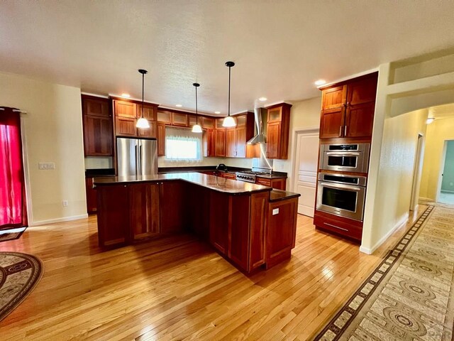 kitchen with stainless steel appliances, a kitchen island, wall chimney range hood, dark countertops, and pendant lighting