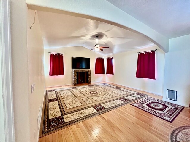 unfurnished living room featuring arched walkways, a fireplace, lofted ceiling, a ceiling fan, and wood finished floors