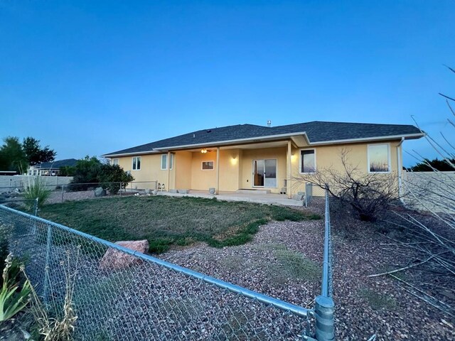 rear view of property with a patio, stucco siding, a shingled roof, a lawn, and a fenced backyard