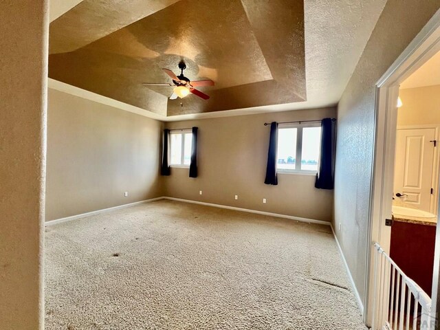 carpeted spare room featuring a raised ceiling, a textured wall, ceiling fan, a textured ceiling, and baseboards