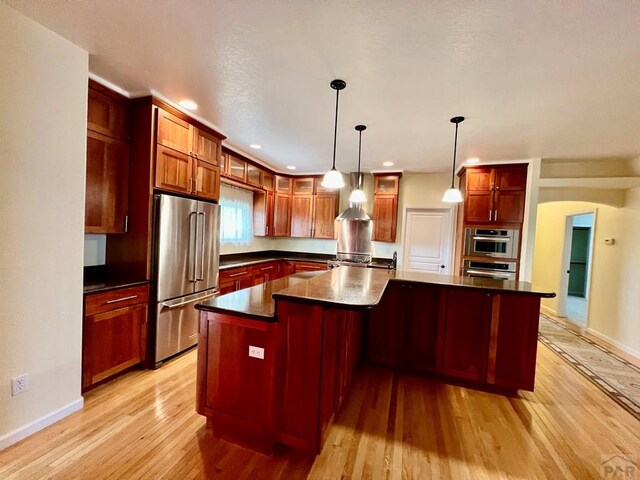 kitchen featuring dark countertops, light wood-style flooring, a kitchen island, decorative light fixtures, and stainless steel appliances