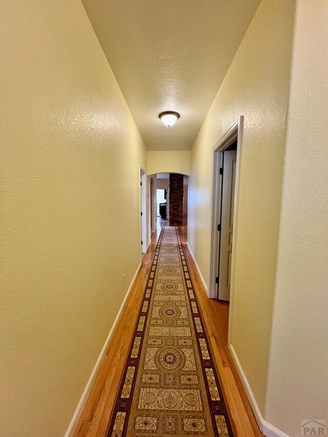 hallway featuring baseboards, arched walkways, and wood finished floors