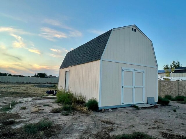 outdoor structure at dusk with a storage shed, fence, and an outbuilding