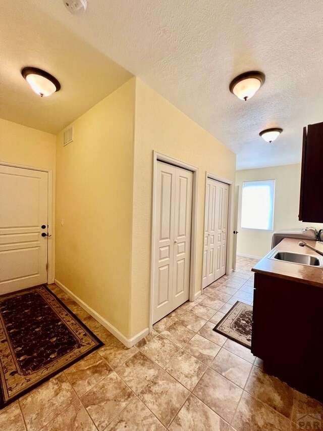 interior space with a textured ceiling, light tile patterned floors, a sink, and baseboards