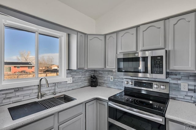 kitchen featuring light stone counters, a sink, appliances with stainless steel finishes, gray cabinets, and decorative backsplash