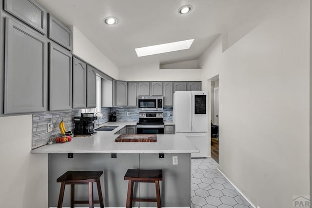 kitchen featuring stainless steel appliances, a breakfast bar, light countertops, and a peninsula