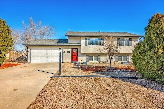 split level home with a garage, fence, concrete driveway, and stucco siding