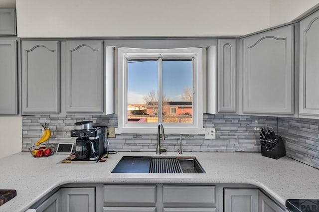 kitchen with light stone counters, decorative backsplash, a sink, and gray cabinetry