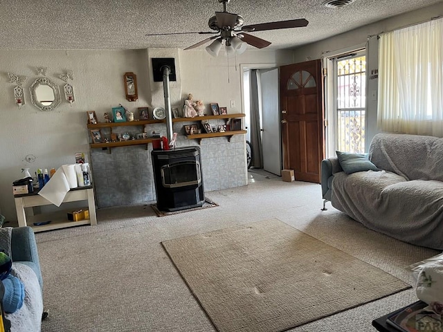 living area with a textured ceiling, a wood stove, ceiling fan, light carpet, and a textured wall