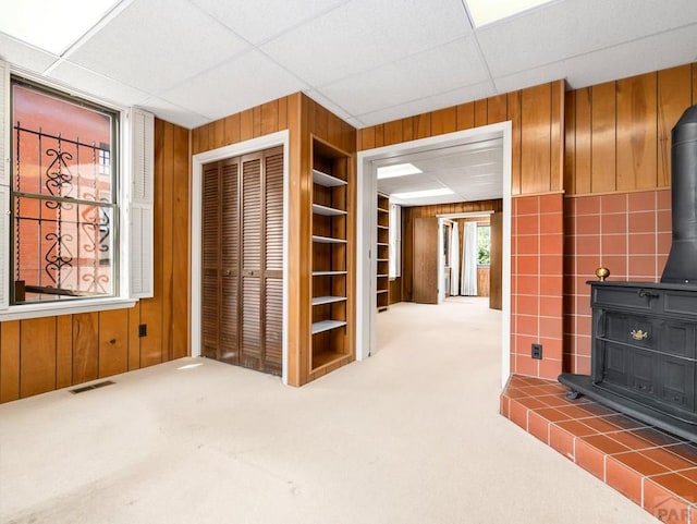 215 E Pitkin Ave, Pueblo, CO 81004 - unfurnished living room featuring a wood stove, wood walls, built in features, carpet floors, and a paneled ceiling