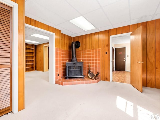 215 E Pitkin Ave, Pueblo, CO 81004 - unfurnished living room with a wood stove, carpet flooring, wood walls, built in shelves, and a paneled ceiling