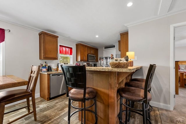 999 Fortino Blvd Unit 237, Pueblo, CO 81008 - kitchen featuring stainless steel appliances, ornamental molding, wood finished floors, a breakfast bar, and brown cabinetry